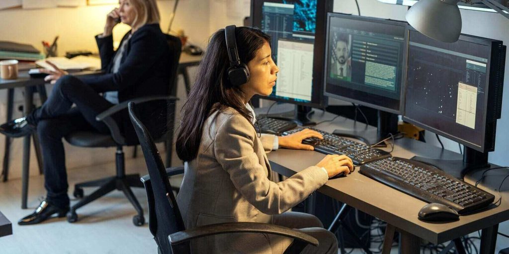female agent of intelligence service sitting in front of computer monitors in office and processing personal data of criminals