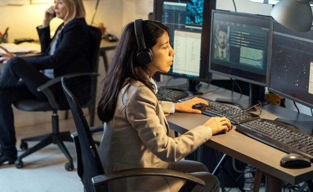 female agent of intelligence service sitting in front of computer monitors in office and processing personal data of criminals