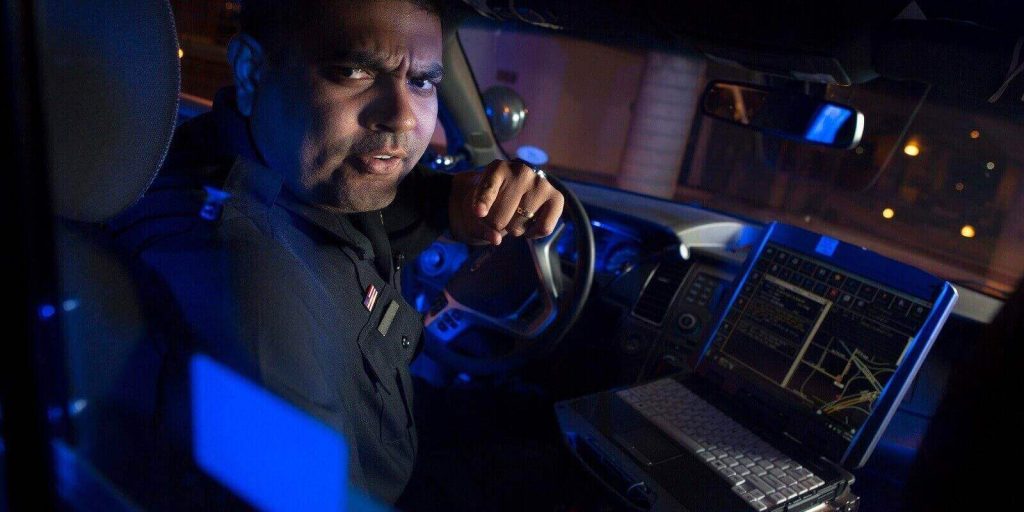 policeman in police car point to back seat