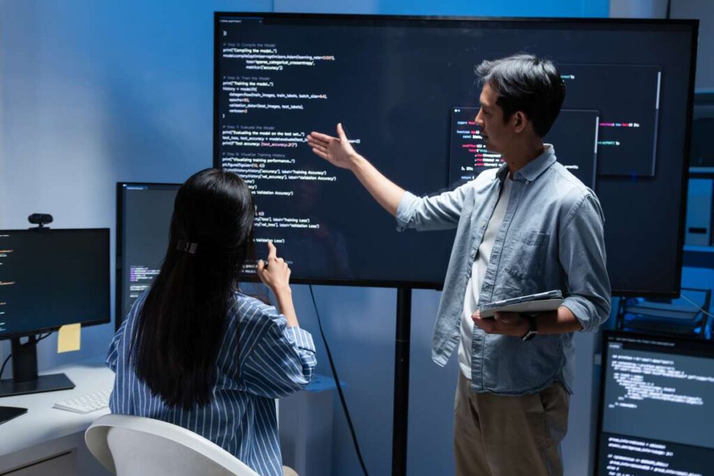 Software Developer Team working late in office at night. Programmer team collaboration, working on coding task, reviewing code while Male Programmer presenting code in the screen in tech office.