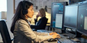female operator of surveillance system sitting by desk in front of computer monitors in office