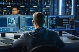 IT Specialist Works on Personal Computer with Screens Showing Software Program with Coding Language Interface. In the Background Technical Room of Data Center with Professional Working