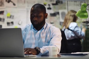 african detective processing evidence working on laptop in office
