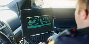 database, laptop and a police officer in a car for security, urban law and safety data while working