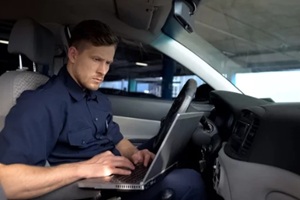 male police officer working on laptop in car, filling data in crime report