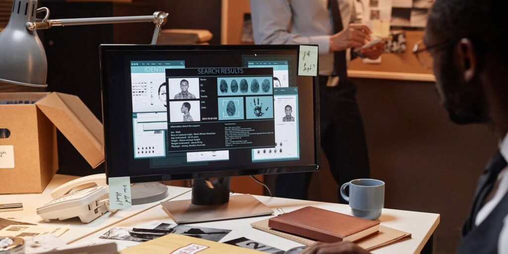 closeup of male detective using computer at workplace and reading suspects personal profile on screen, copy space