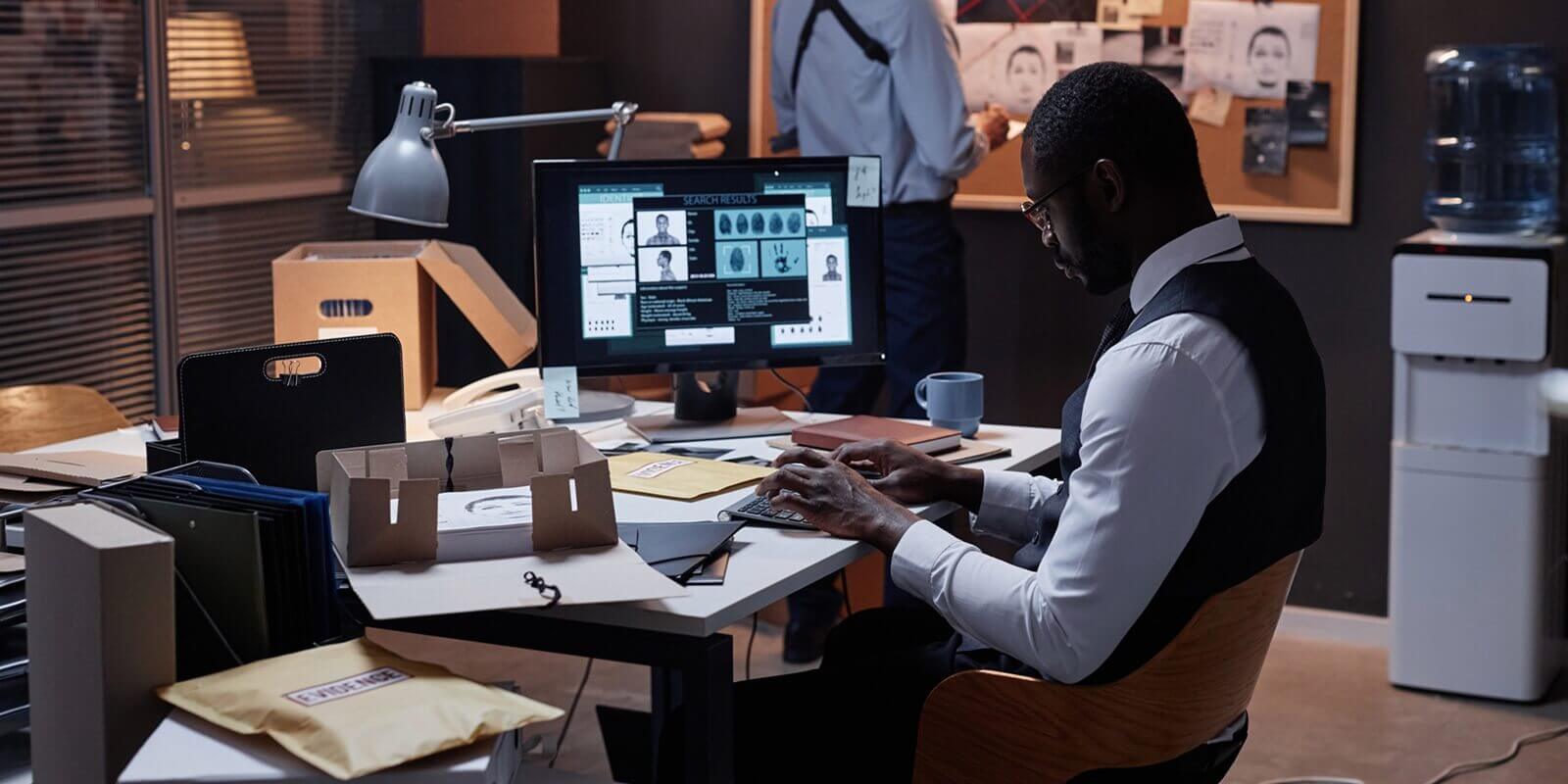 side view portrait of African American male detective using computer at workplace with personal profile - law enforcement grants